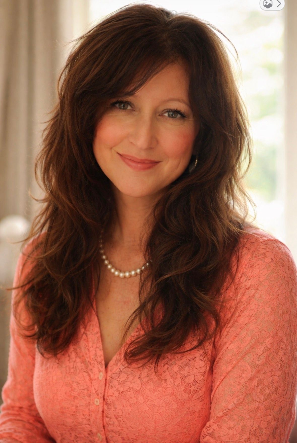 Woman with dark hair, smiling, wearing a green top and silver necklace against a gray background.