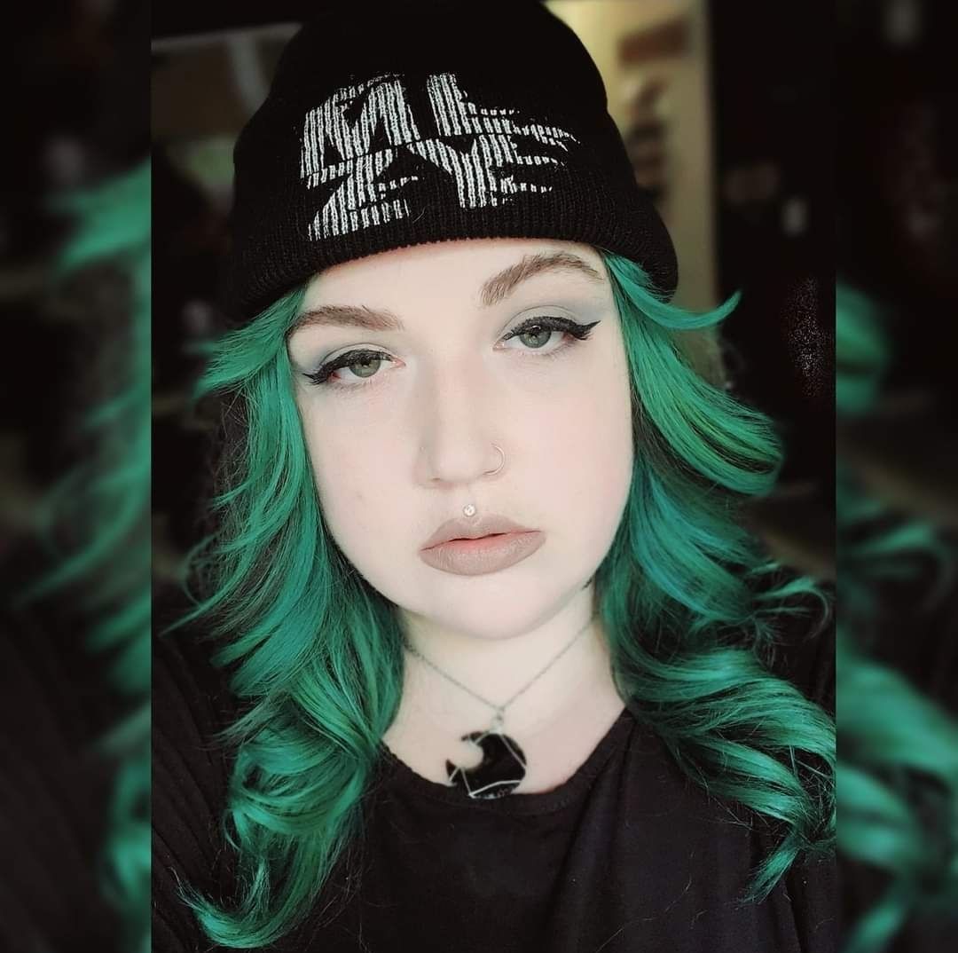 Person with green hair, black beanie, and black necklace, looking at the camera.