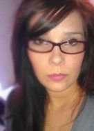 Woman with dark hair and glasses looking forward, close-up.