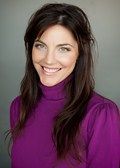 Woman smiling, wearing a purple turtleneck, dark hair, neutral background.
