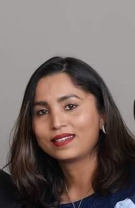 Woman with dark hair smiles, wearing a dark blue top, against a gray background.