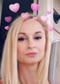 Woman with long blonde hair, wearing a heart filter; looking at camera.