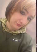 Woman with light brown and blonde hair, wearing a green hooded sweatshirt, looking at the camera.