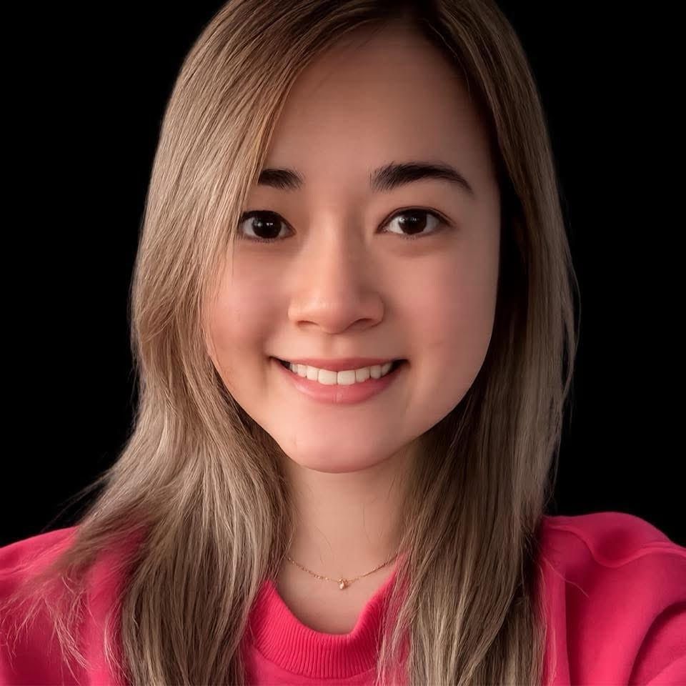 Woman with blonde-highlighted hair smiles, wearing a blue sweater, seated in front of a neutral background.