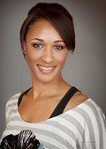Woman with brown hair smiling, wearing striped shirt, studio background.