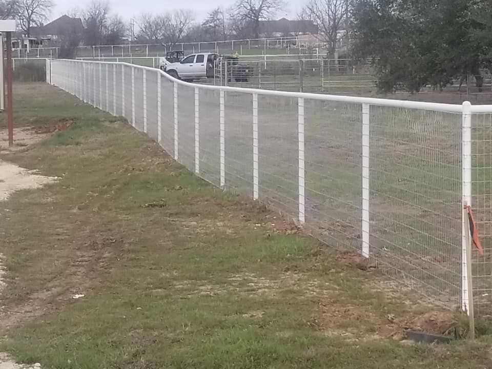 A white fence surrounds a grassy field with a truck parked in the background.