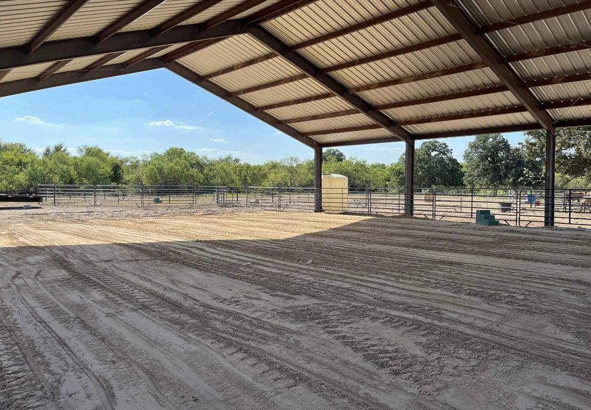 A large covered area with a lot of dirt and trees in the background.