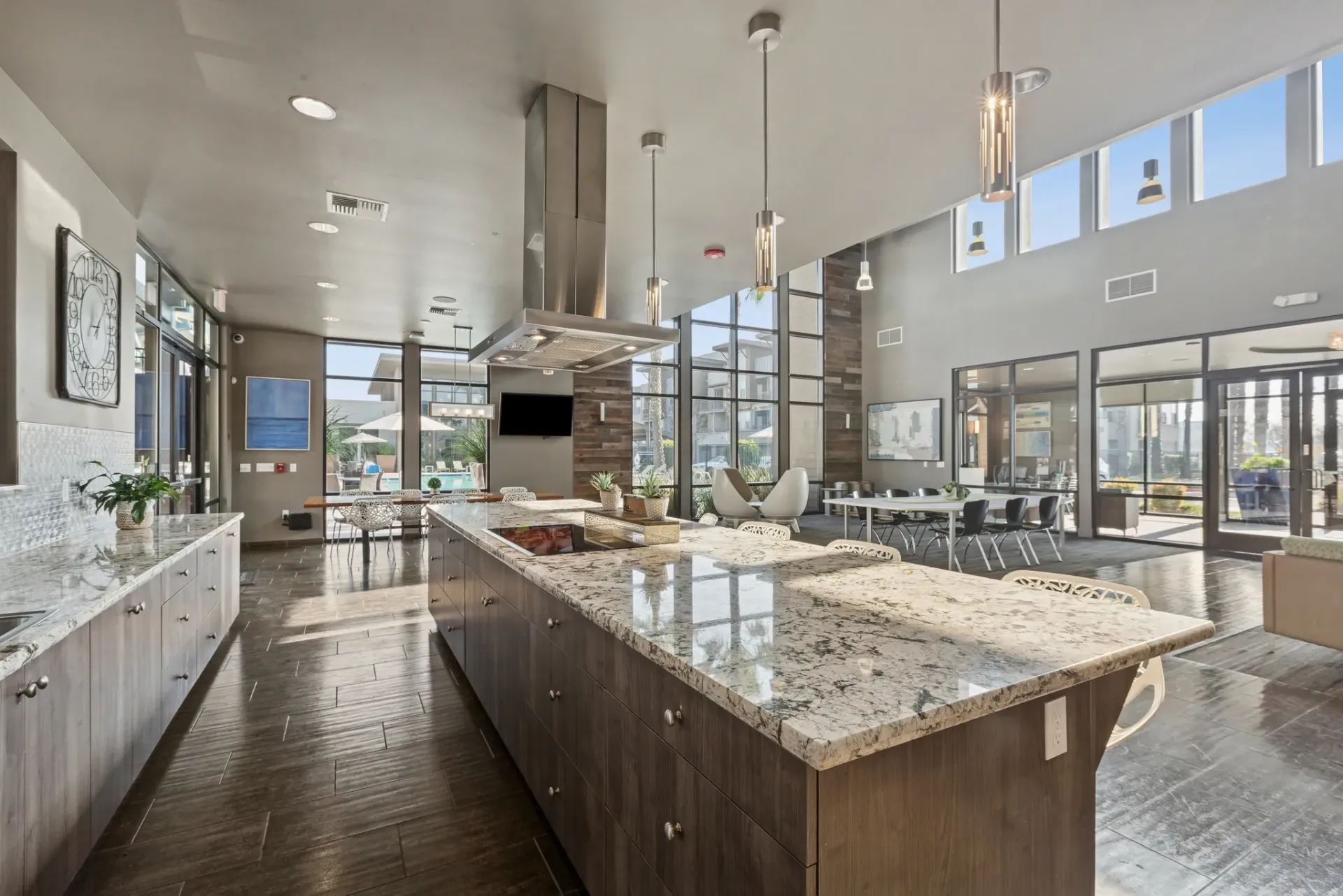 Modern communal kitchen with large island and seating, overlooking a pool area.