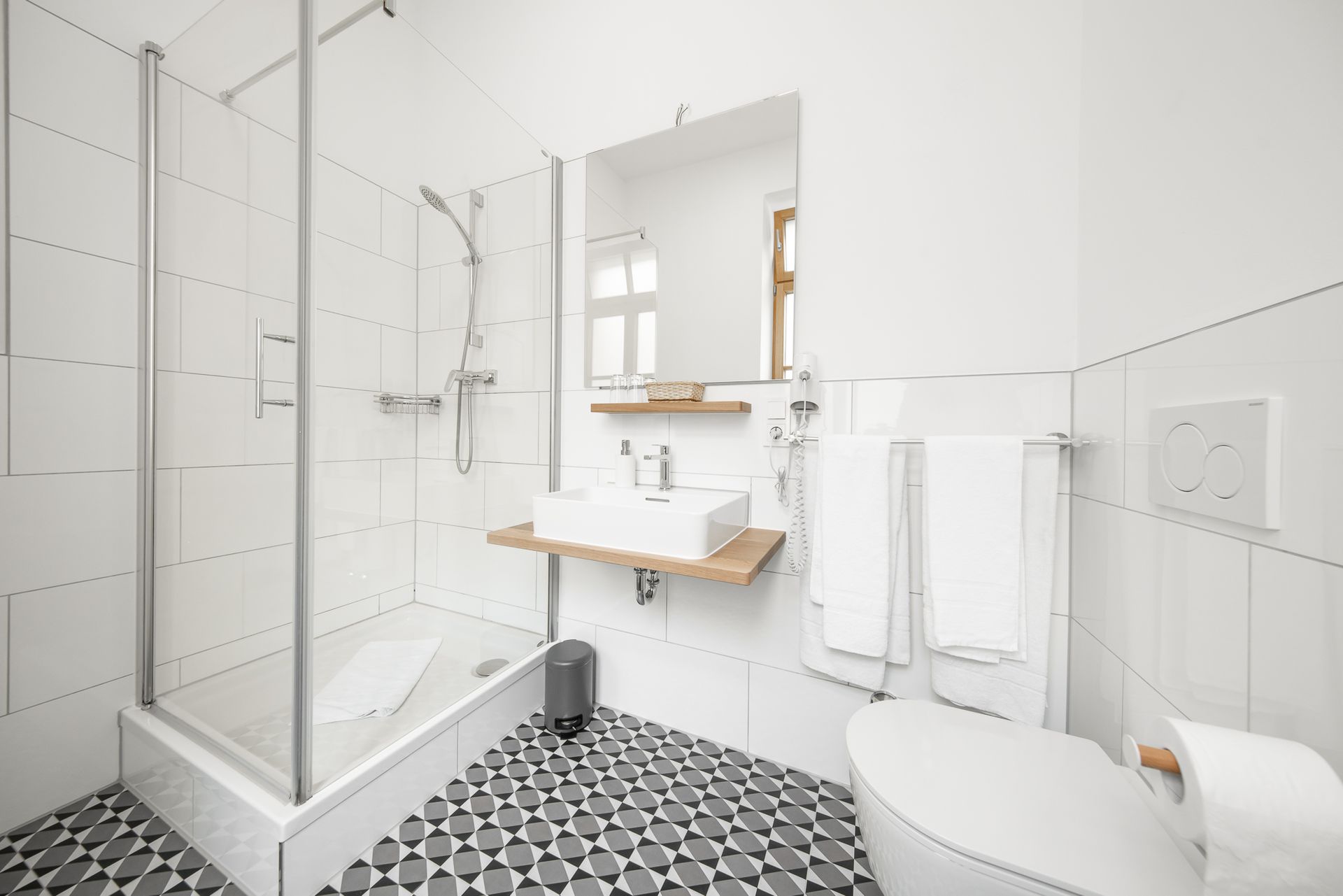 Modern bathroom with white tiled walls, glass shower, and patterned floor.