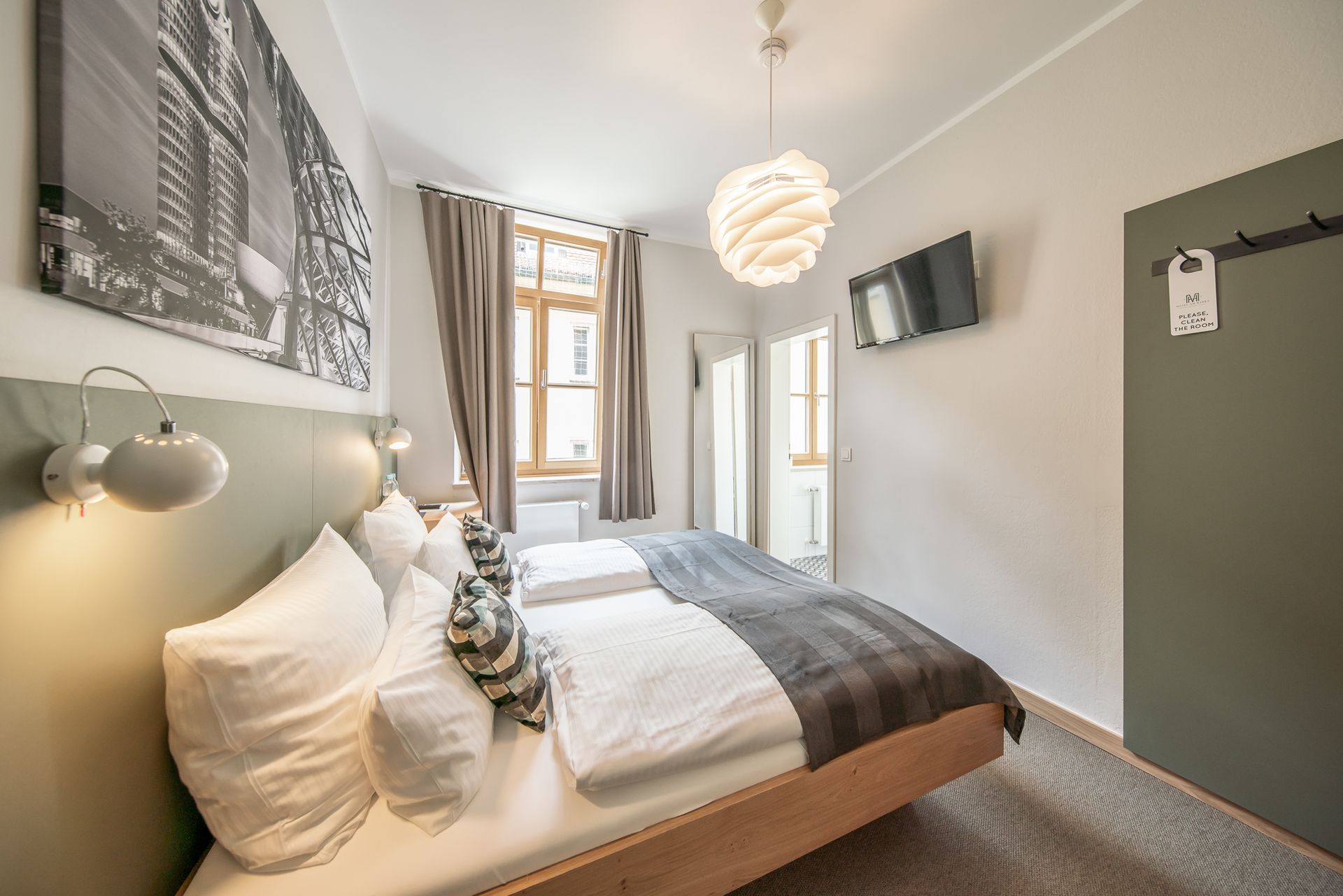 Bedroom with a bed, TV, window, and wall-mounted art. Neutral tones with a modern aesthetic.