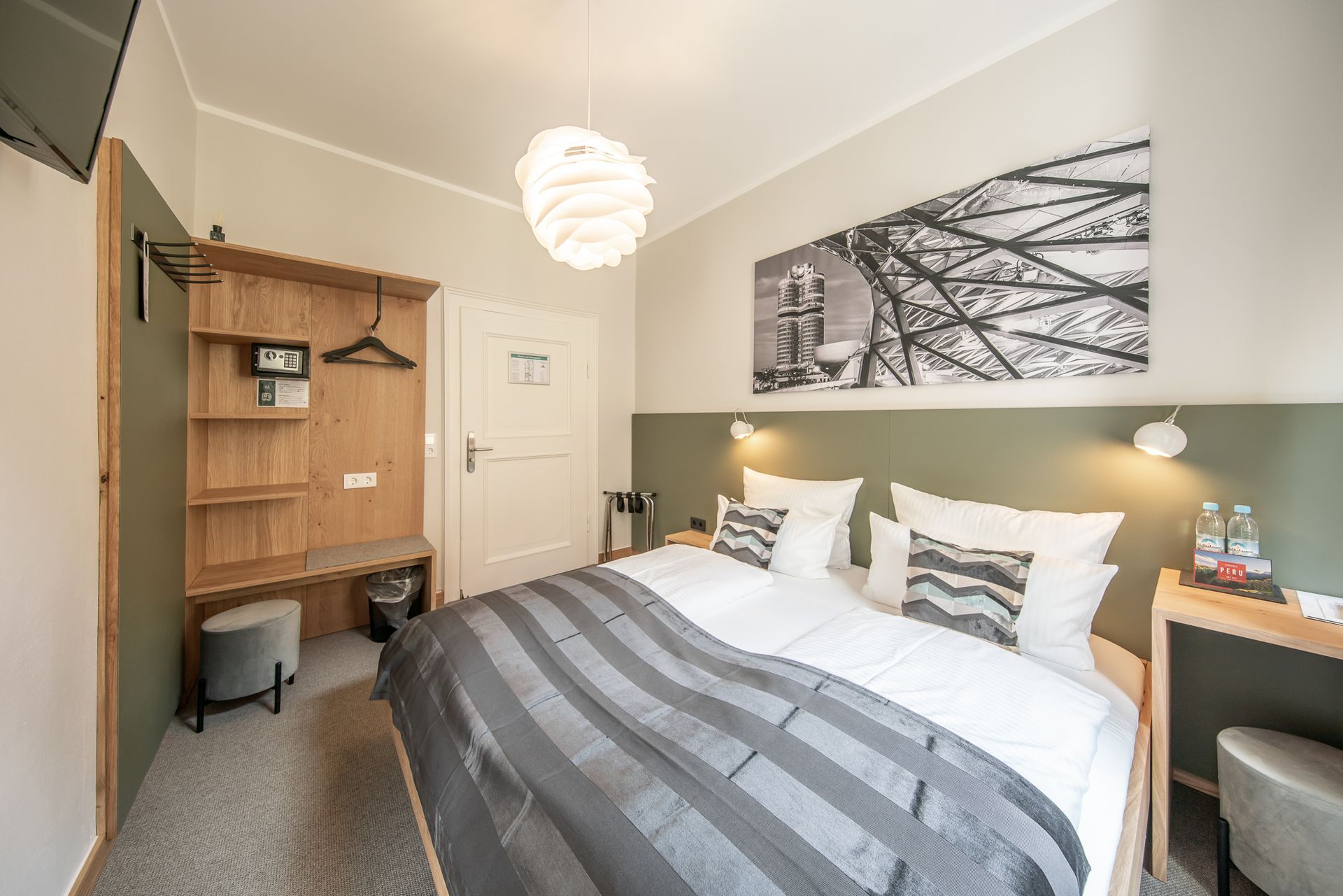 Hotel room with a bed, artwork, a wardrobe, and a small side table.