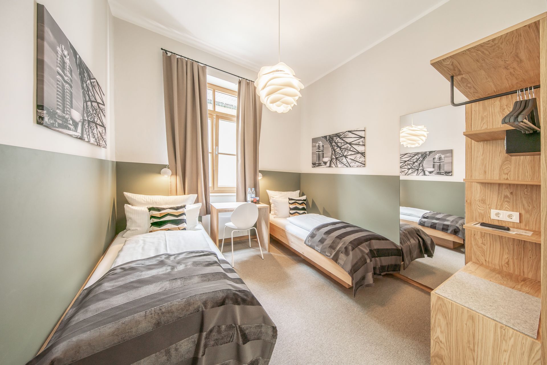 Two twin beds in a bright room with a desk. A mirror and open wardrobe on right.