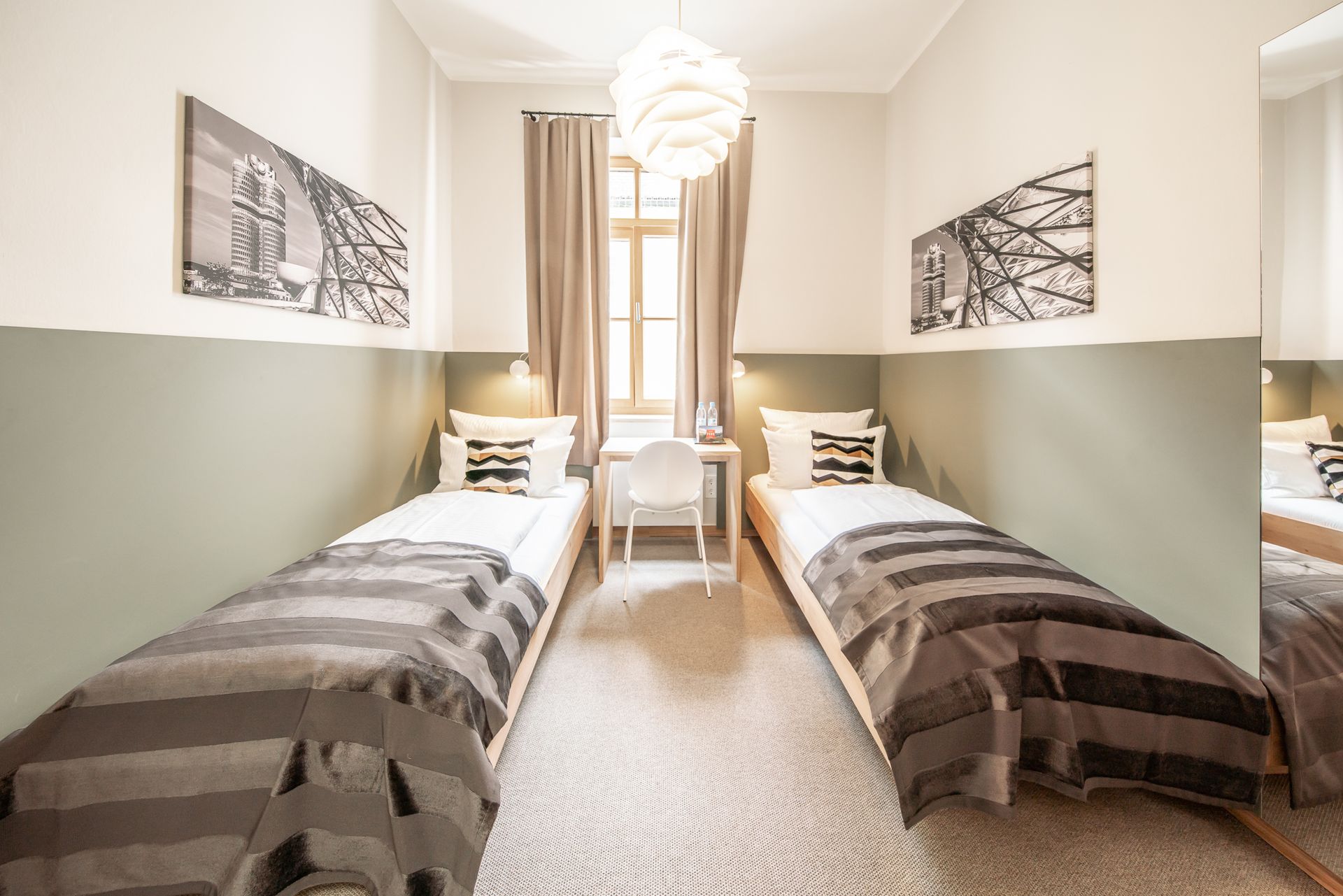 Twin-bedded room with beds, desk, window, artwork, and neutral color scheme.
