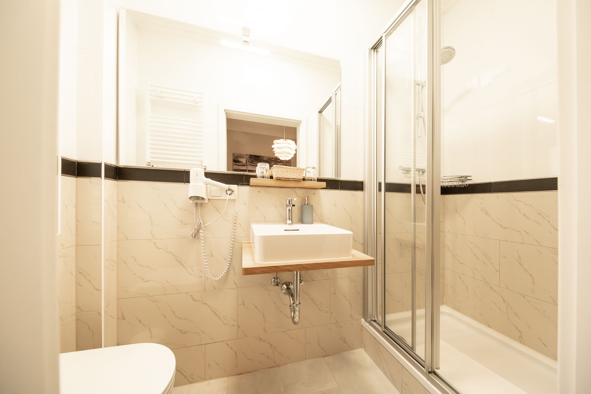 Small bathroom with a white sink, shower, and toilet. The walls are light colored with a dark border.
