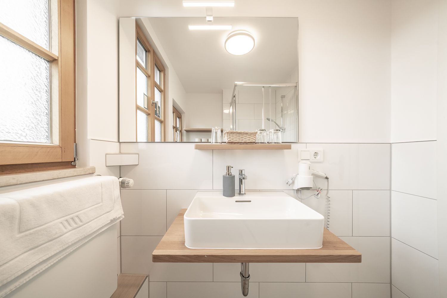 Bathroom with white square sink, wooden shelf, large mirror, and shower stall.