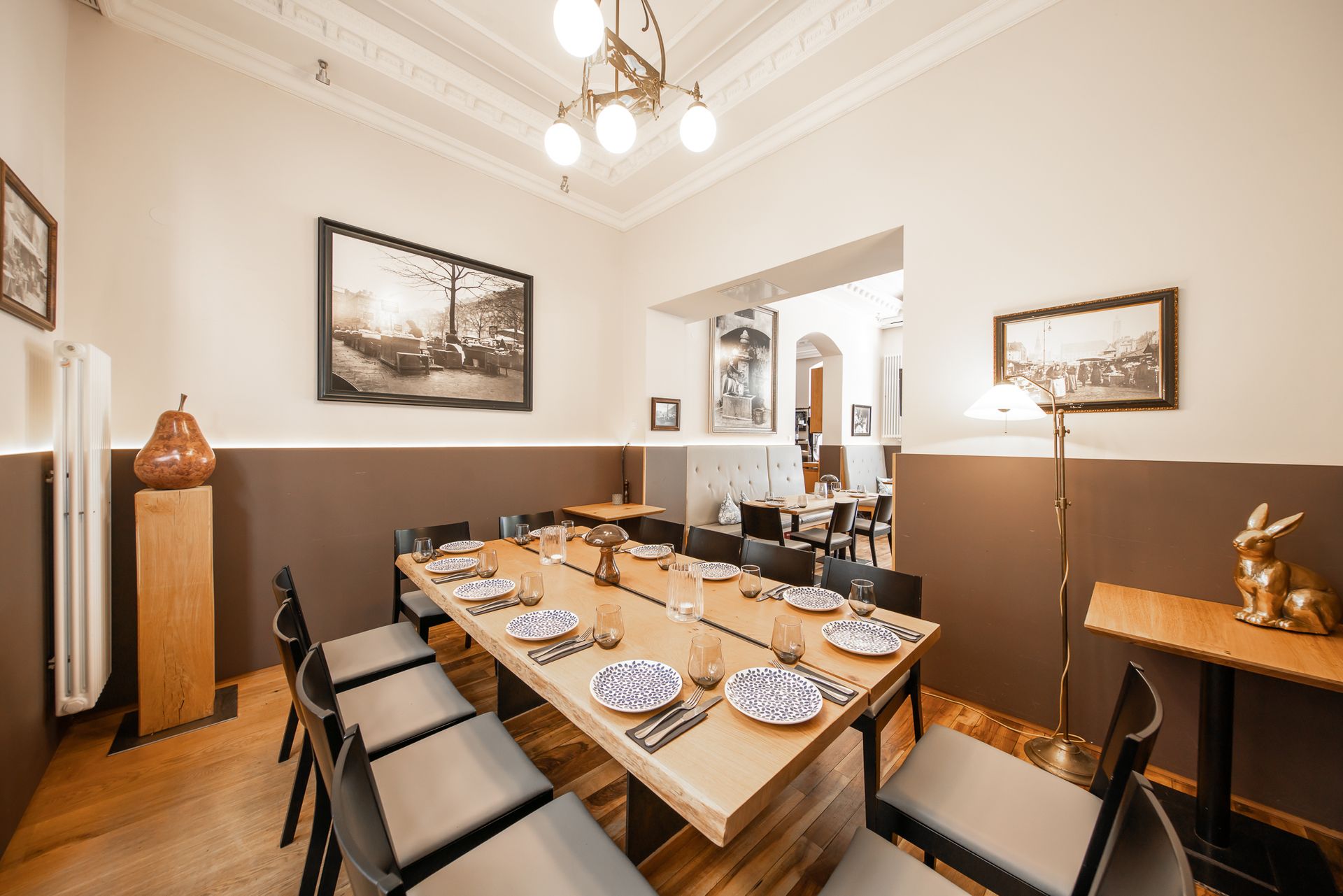 Elegant dining room with long wooden table set for a meal; brown and beige walls, vintage art, ornate ceiling.