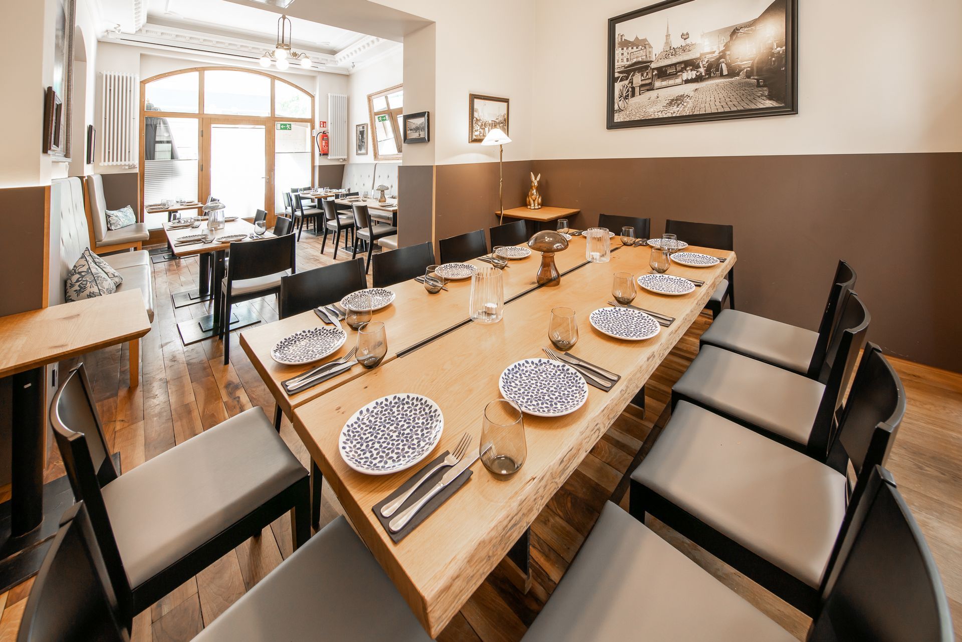 Restaurant dining room with long table set for a meal. Includes chairs, tableware, and a vintage photo.