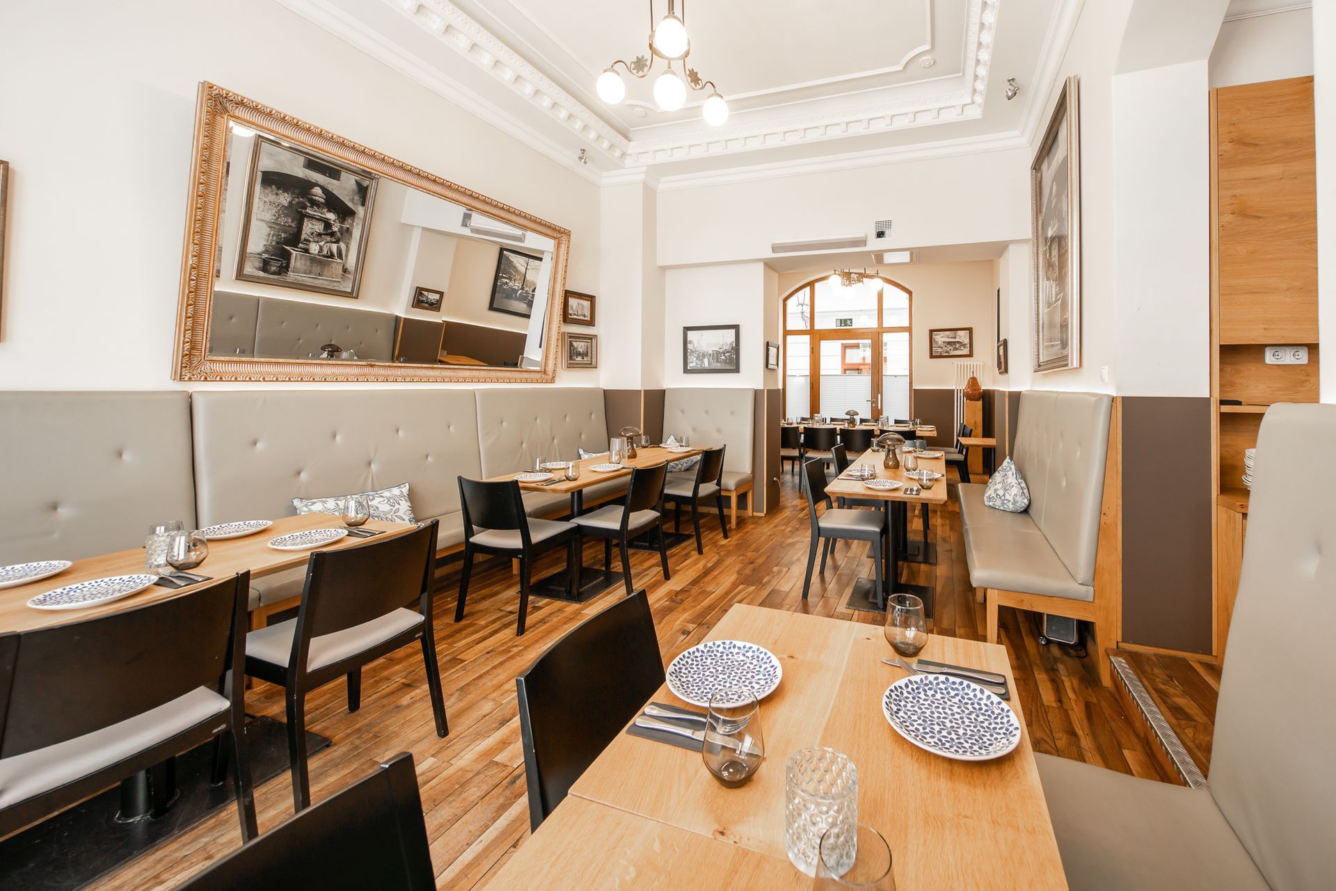 Restaurant interior with tables set for dining, wooden floors, and a large mirror.
