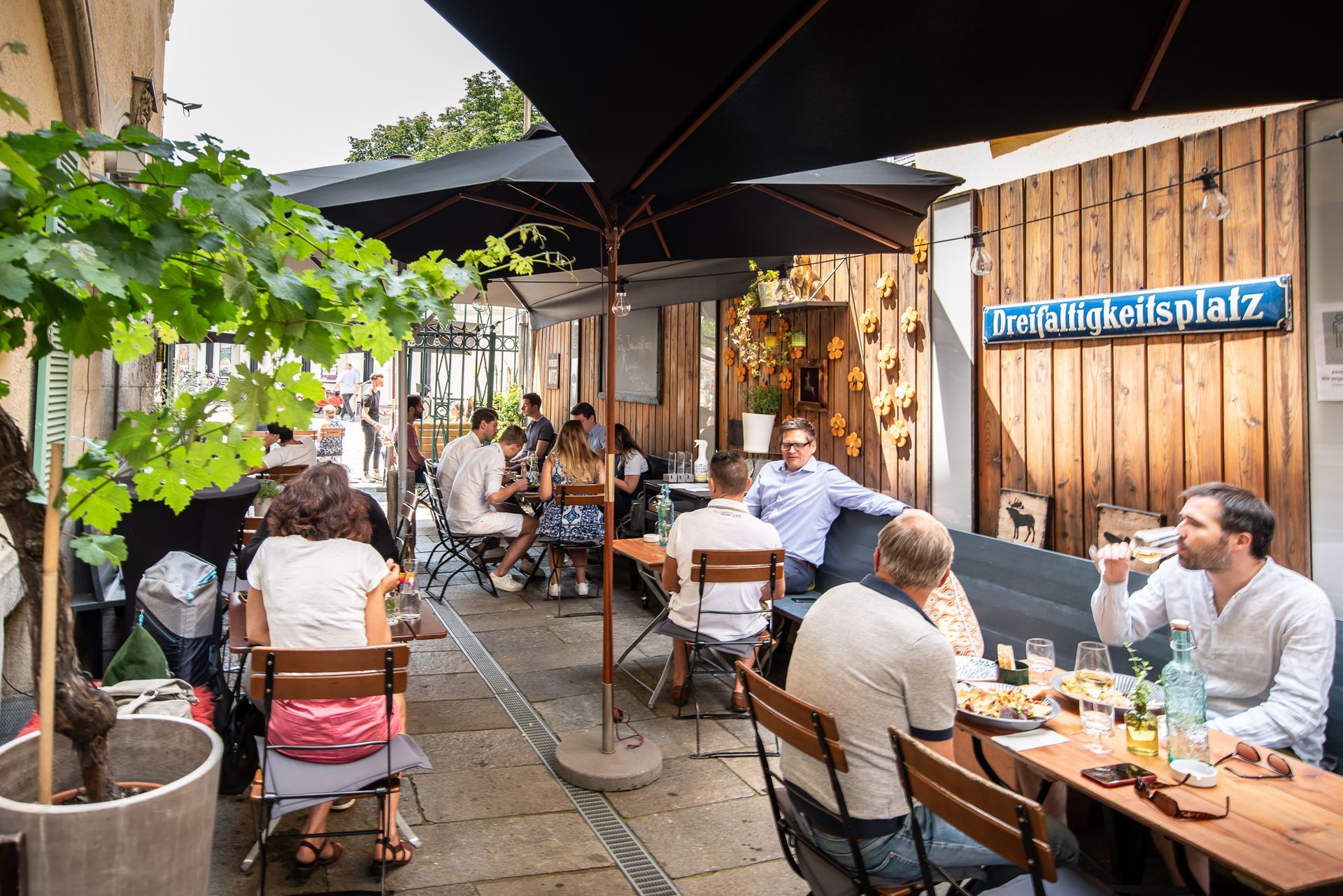 Outdoor restaurant seating; people eating and drinking under black umbrellas.
