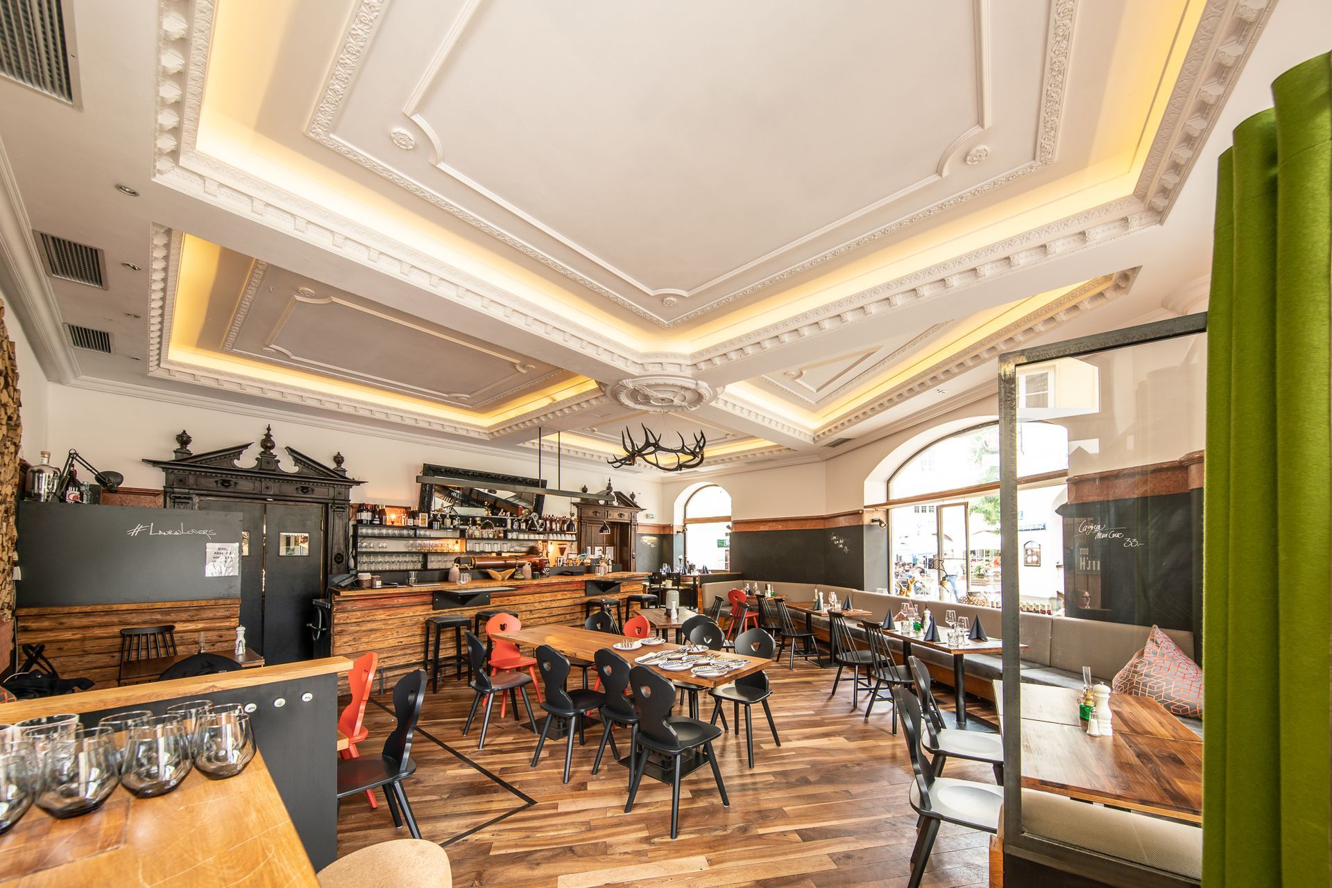 Restaurant interior with ornate ceiling, bar, tables, and chairs.