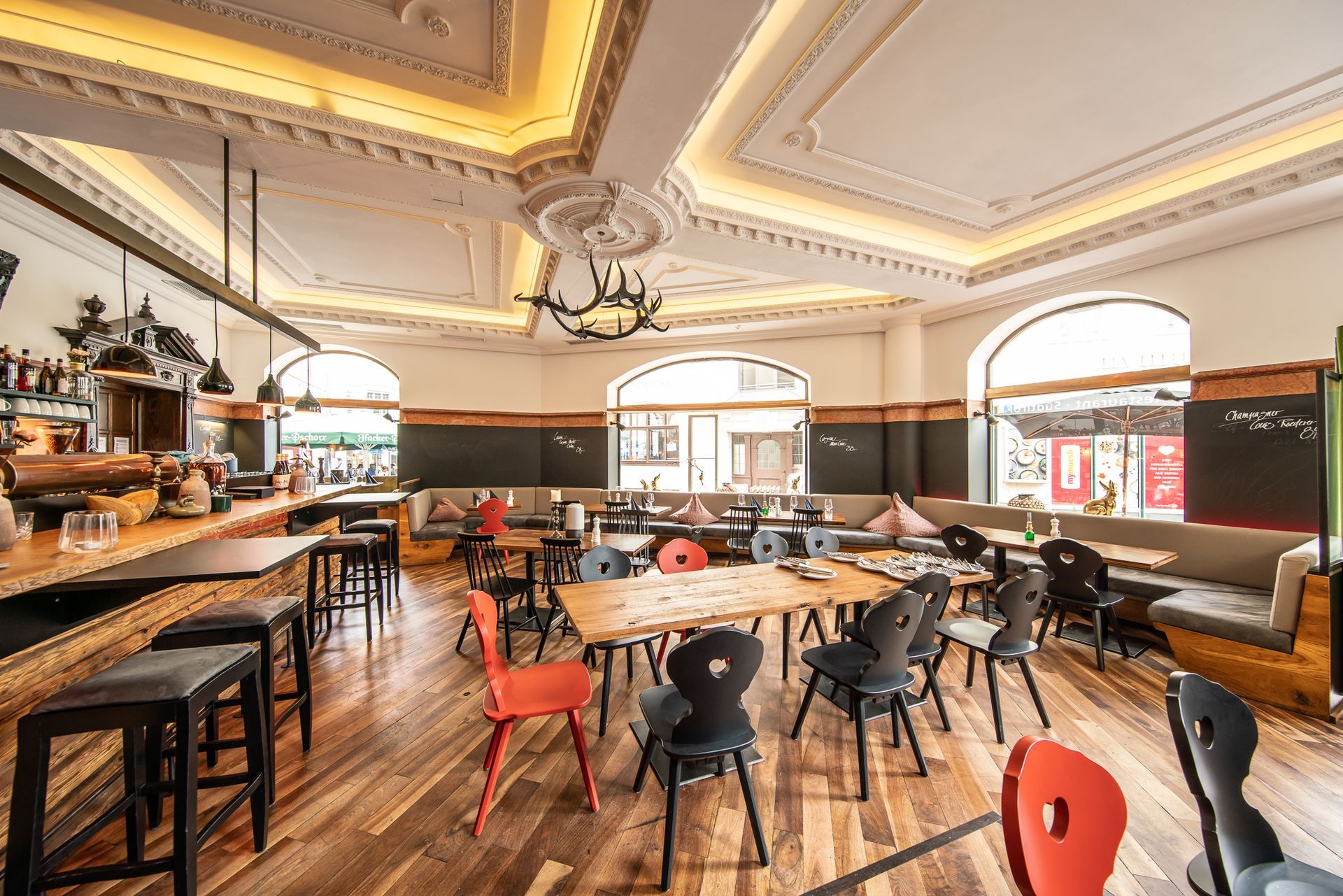 Restaurant interior with wooden floor, tables, chairs, bar, and decorative ceiling.