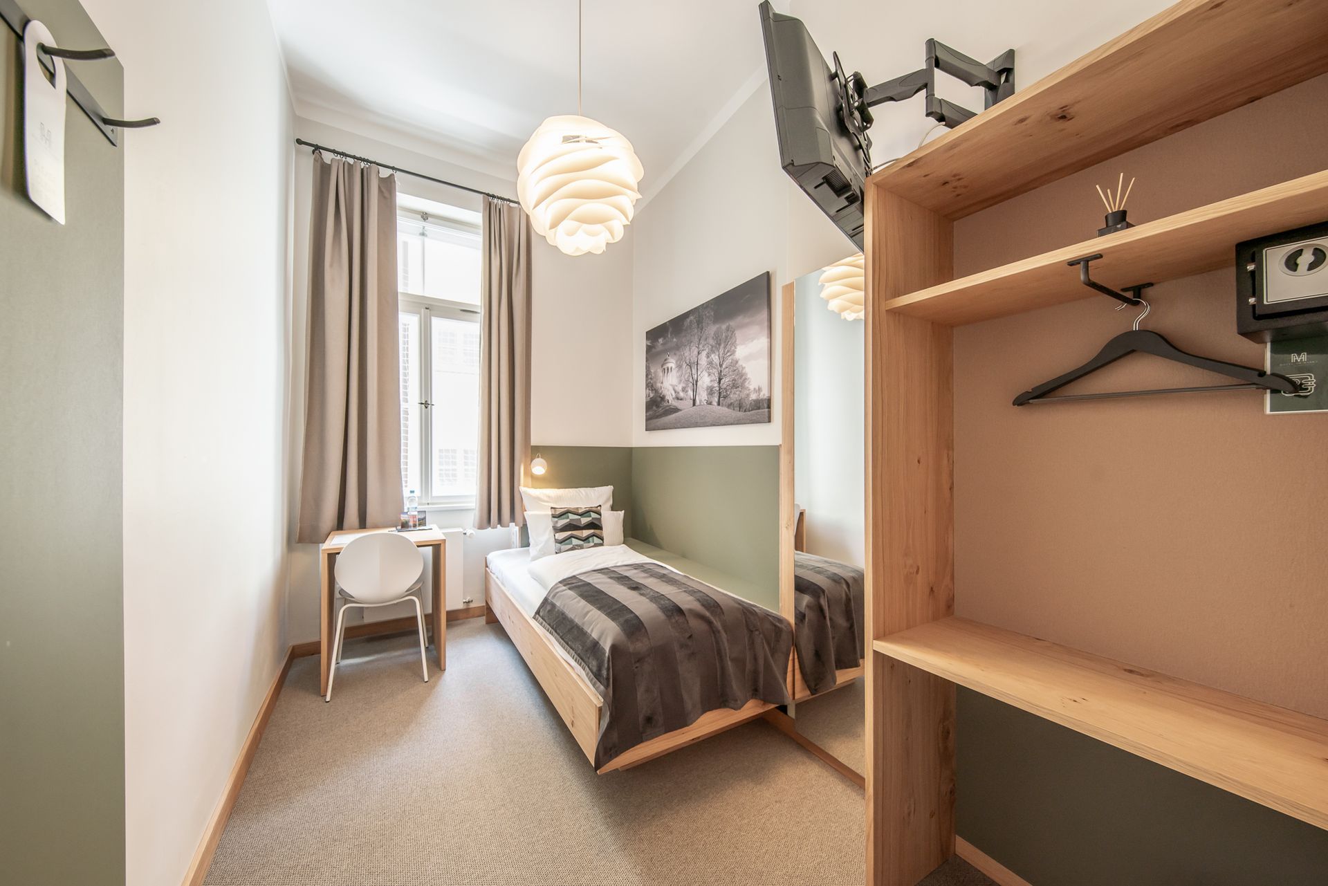 Small hotel room with a single bed, desk, and open closet.