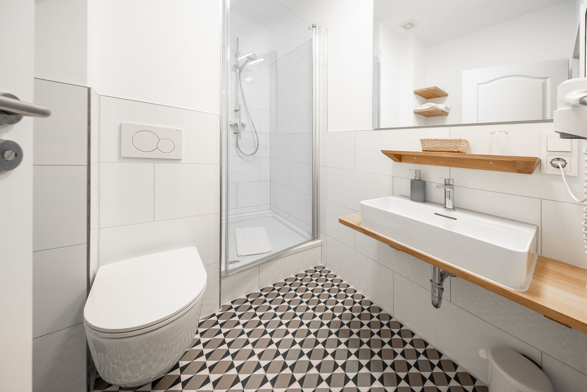 Modern bathroom with a white toilet, sink, and shower. Black, gray, and white floor tiles.