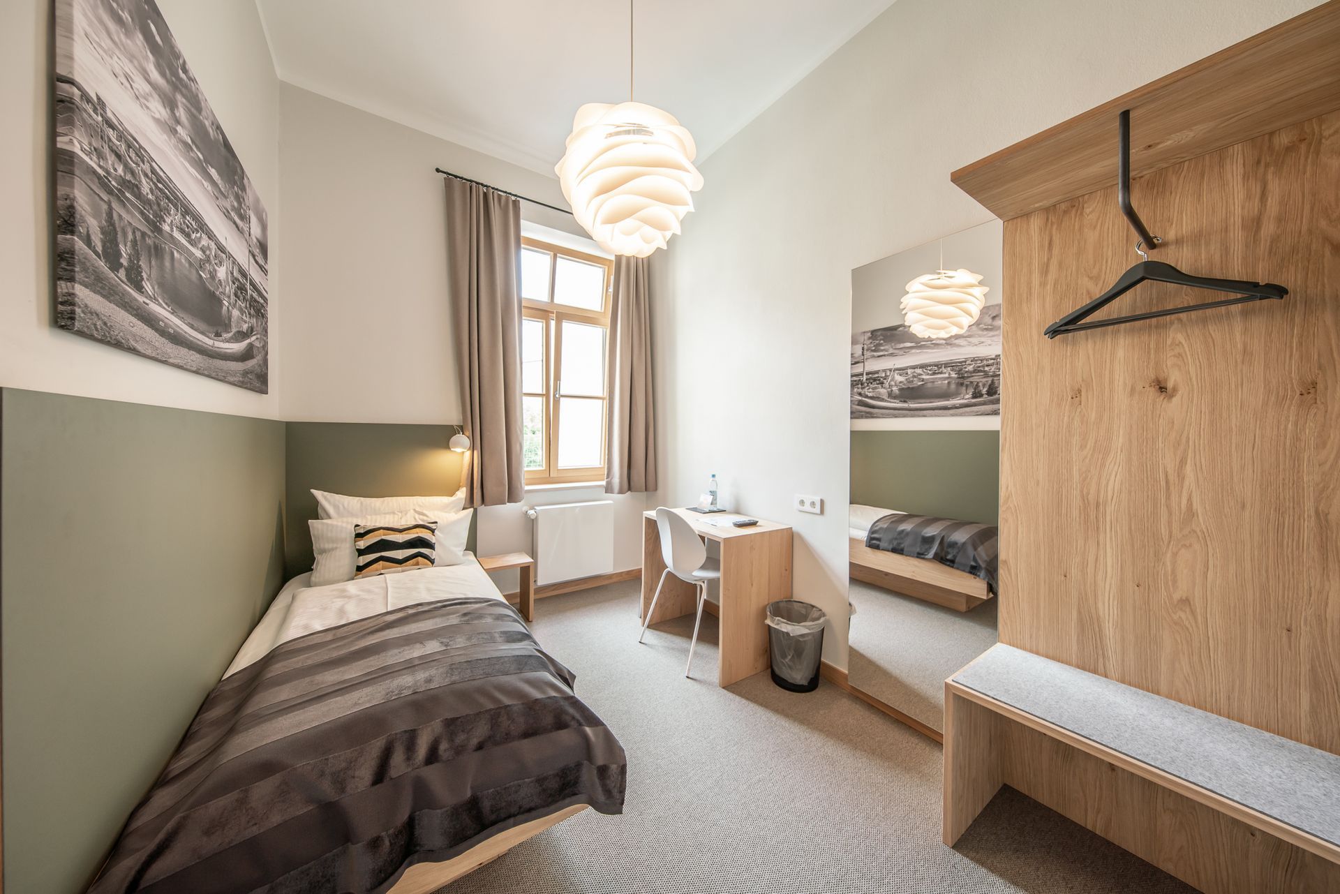 Hotel room with single bed, desk, and wooden closet, neutral tones, and window.