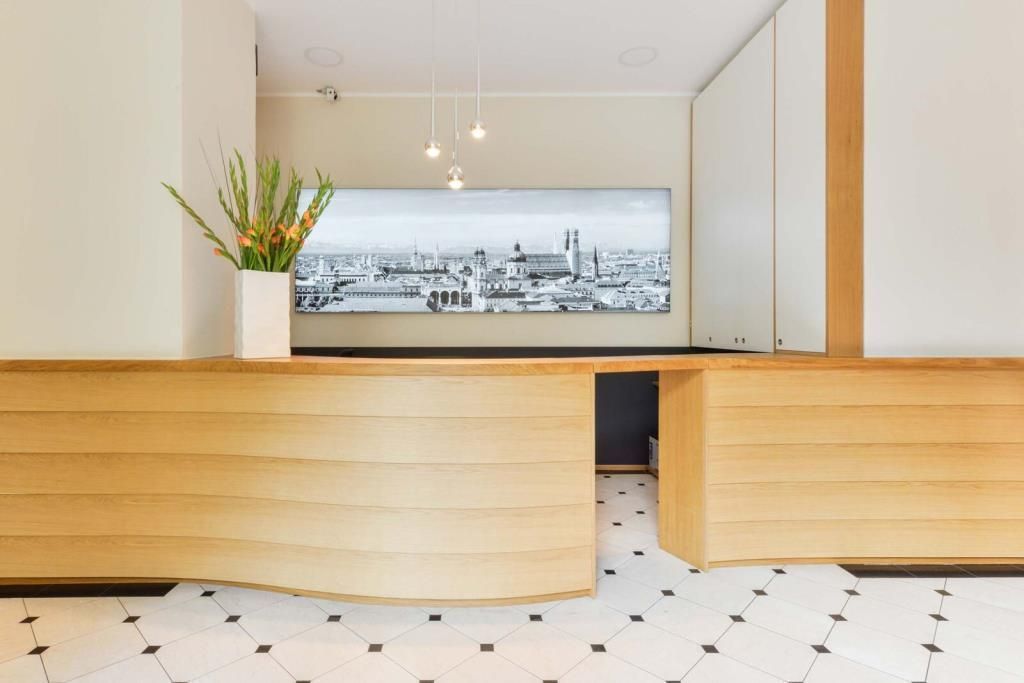 Reception desk with light wood facade, large cityscape art, and floral arrangement. Black and white tiled floor.
