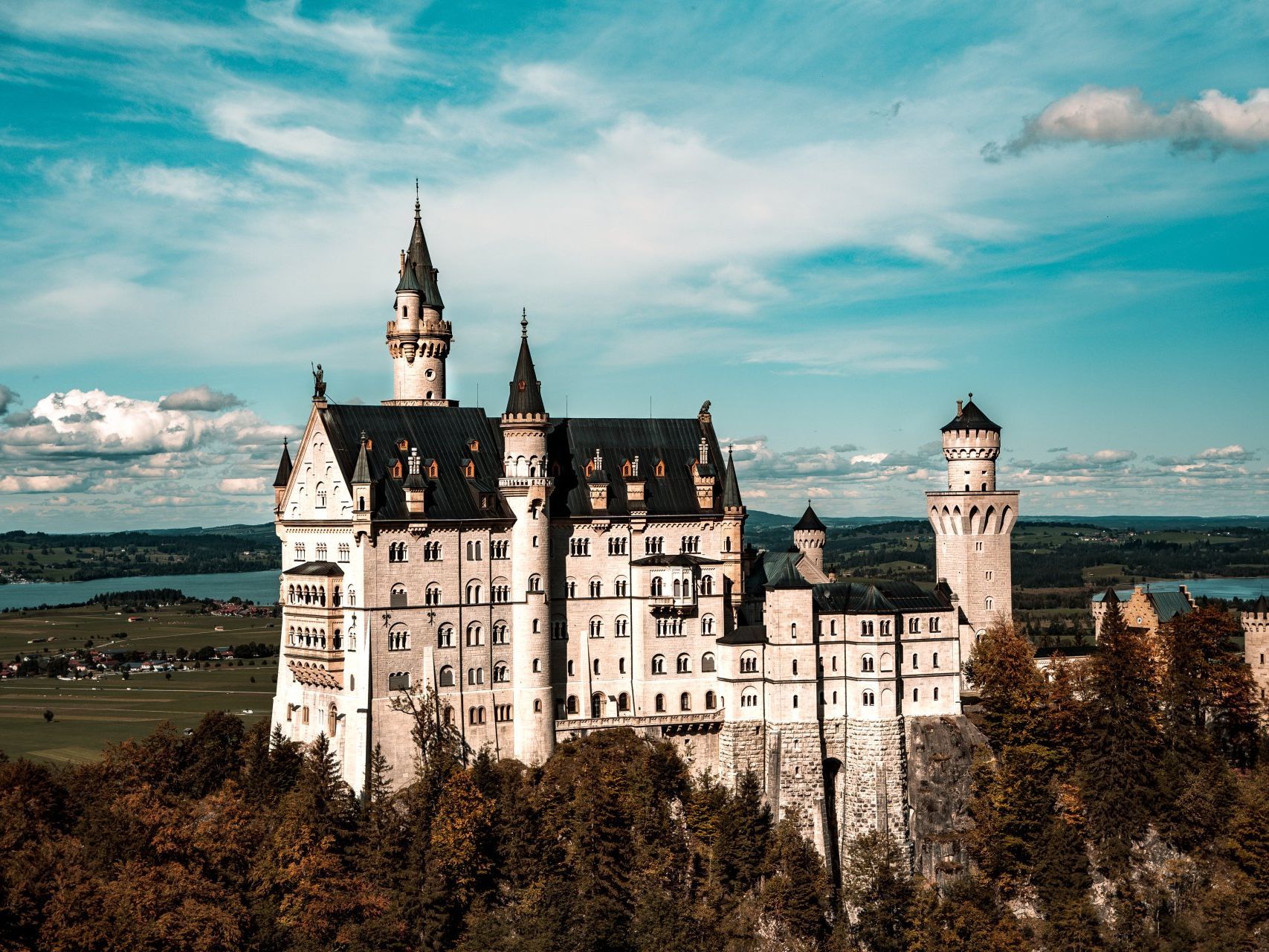 Neuschwanstein Castle, Germany, set atop a hill, with blue sky and some water in the background.