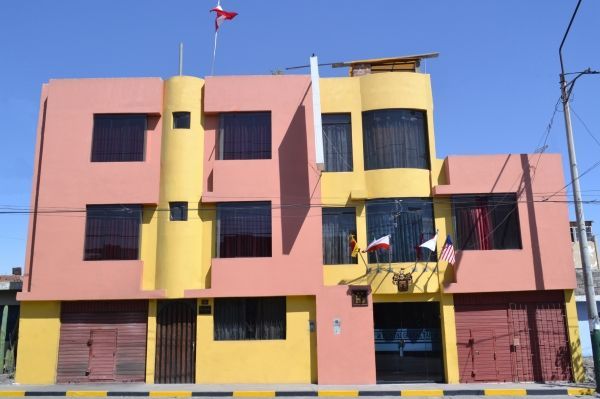 Edificio rosa y amarillo de tres pisos con ventanas enrejadas bajo un cielo azul.