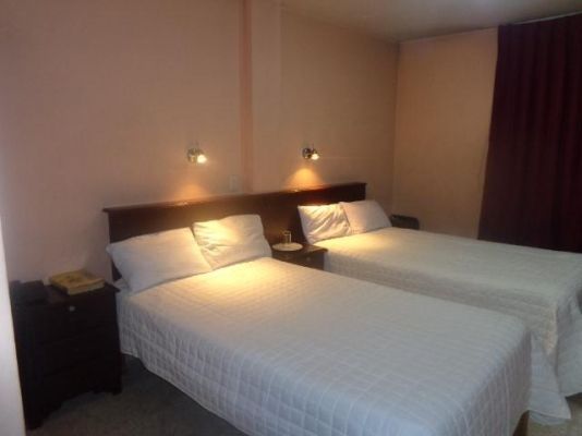 Dos camas individuales bien hechas con ropa de cama blanca en una habitación de hotel con iluminación tenue.