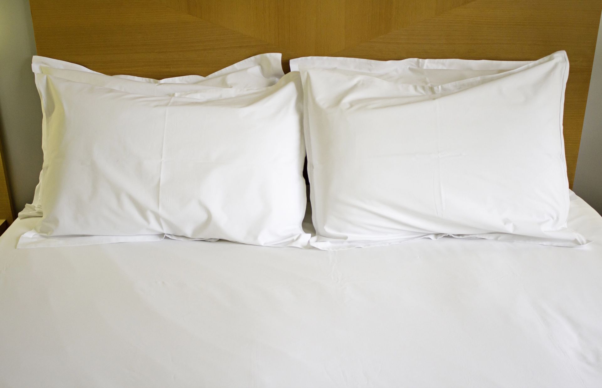 Dos almohadas blancas sobre una cama bien hecha con sábanas blancas, apoyada contra un cabecero de madera.