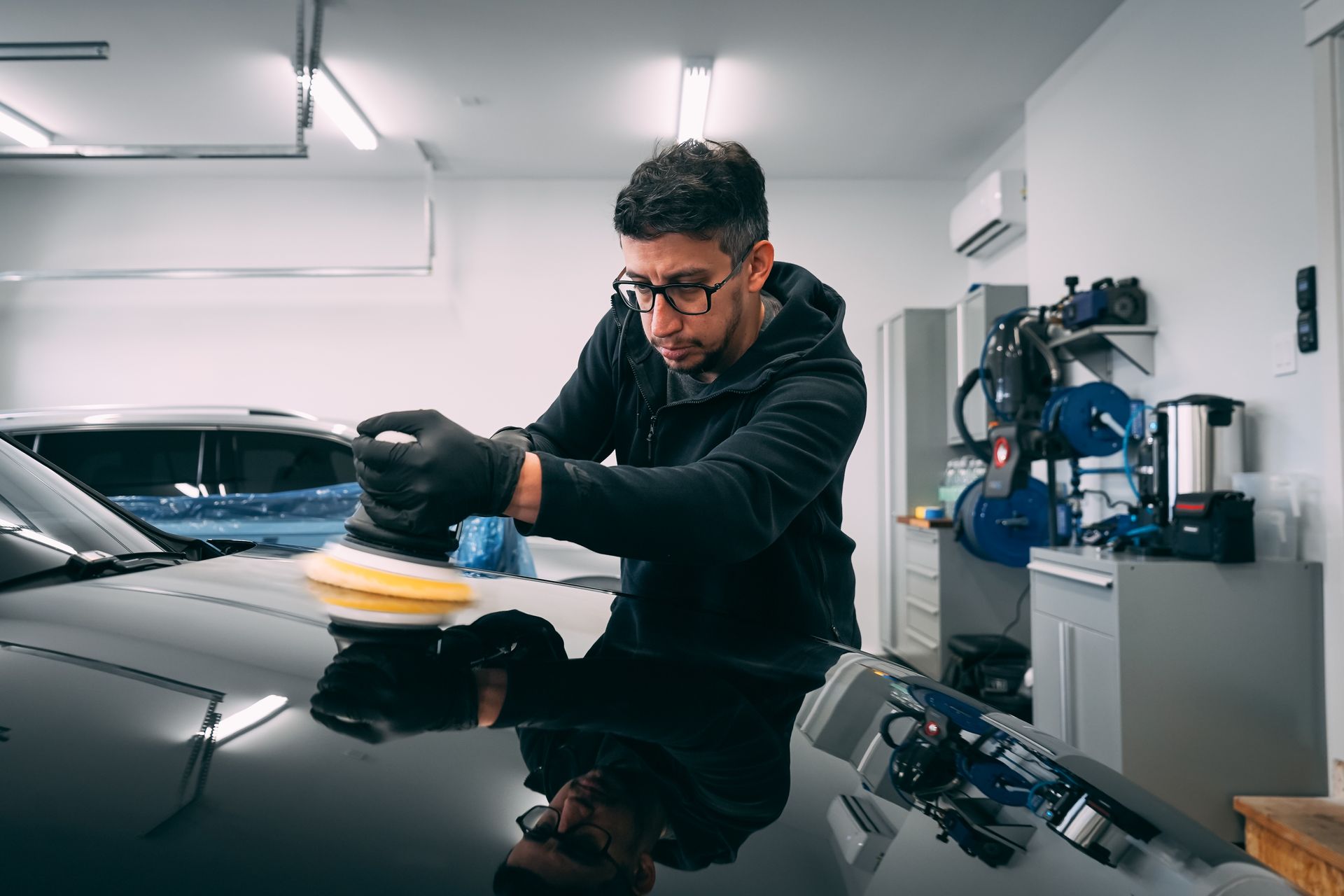 A man is polishing the hood of a car in a garage.