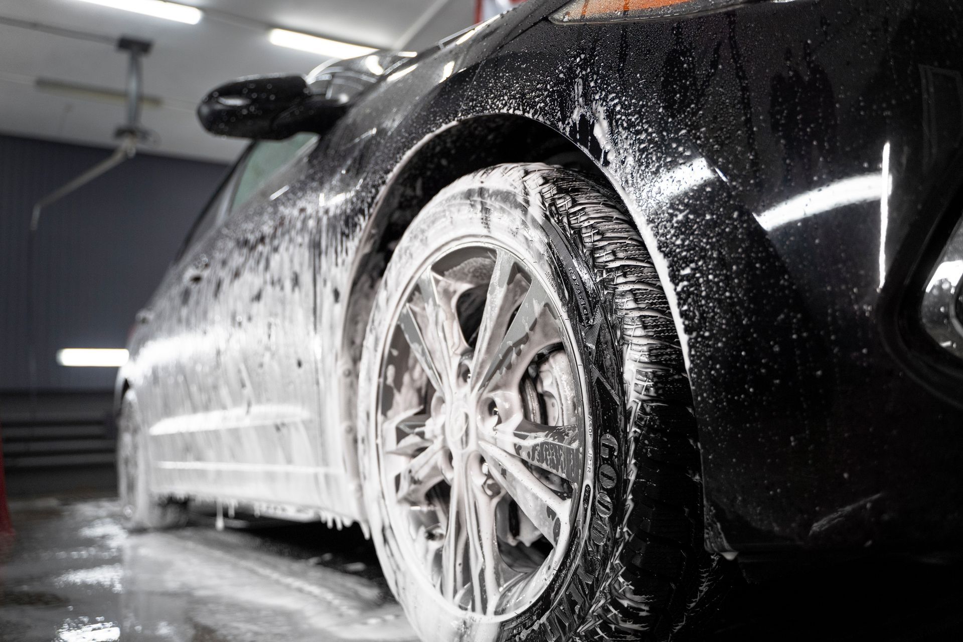 A black car is being washed with soap and water in a garage.