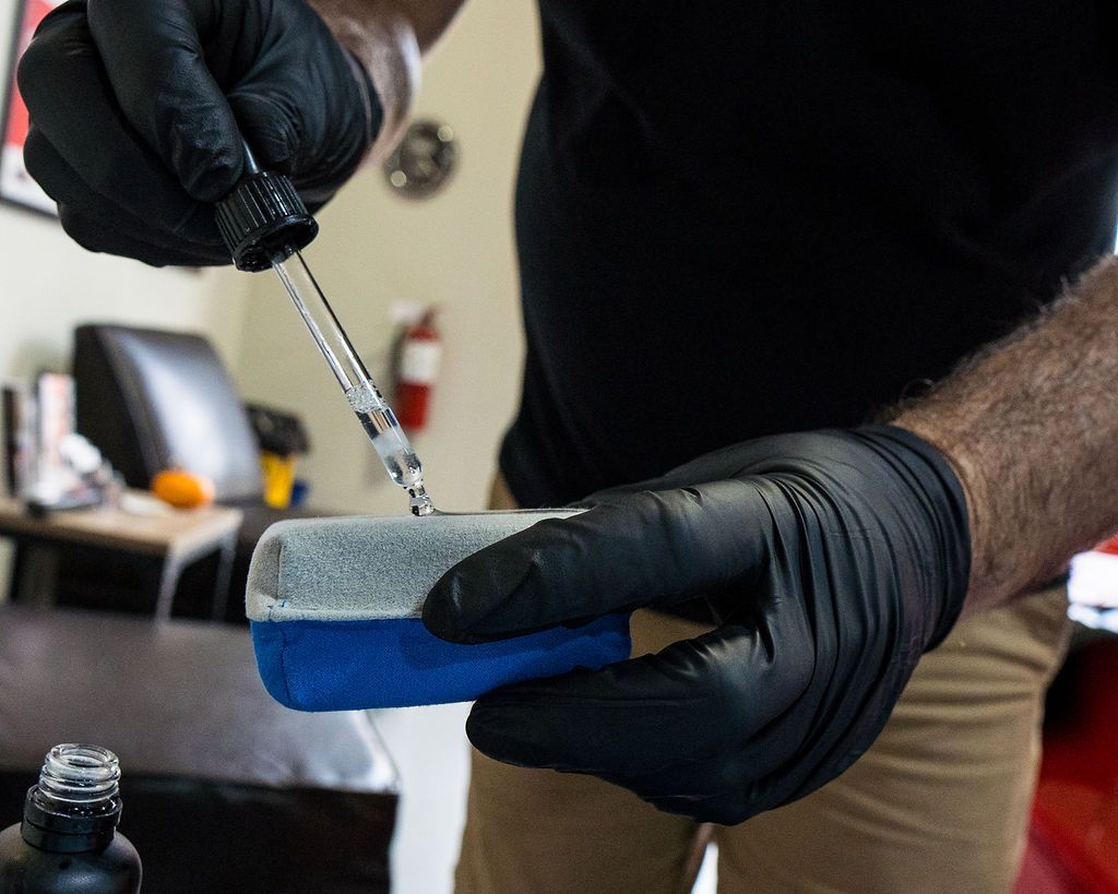 A man wearing black gloves is pouring liquid into a blue sponge.