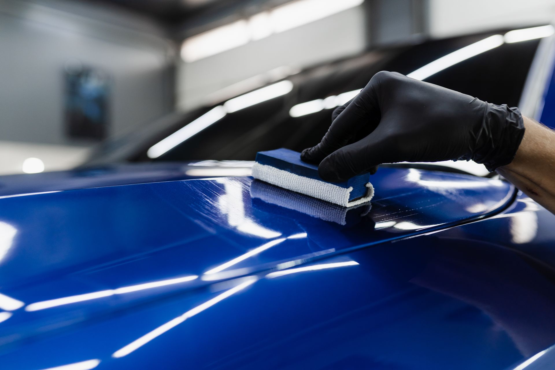 A person is polishing a blue car with a sponge.