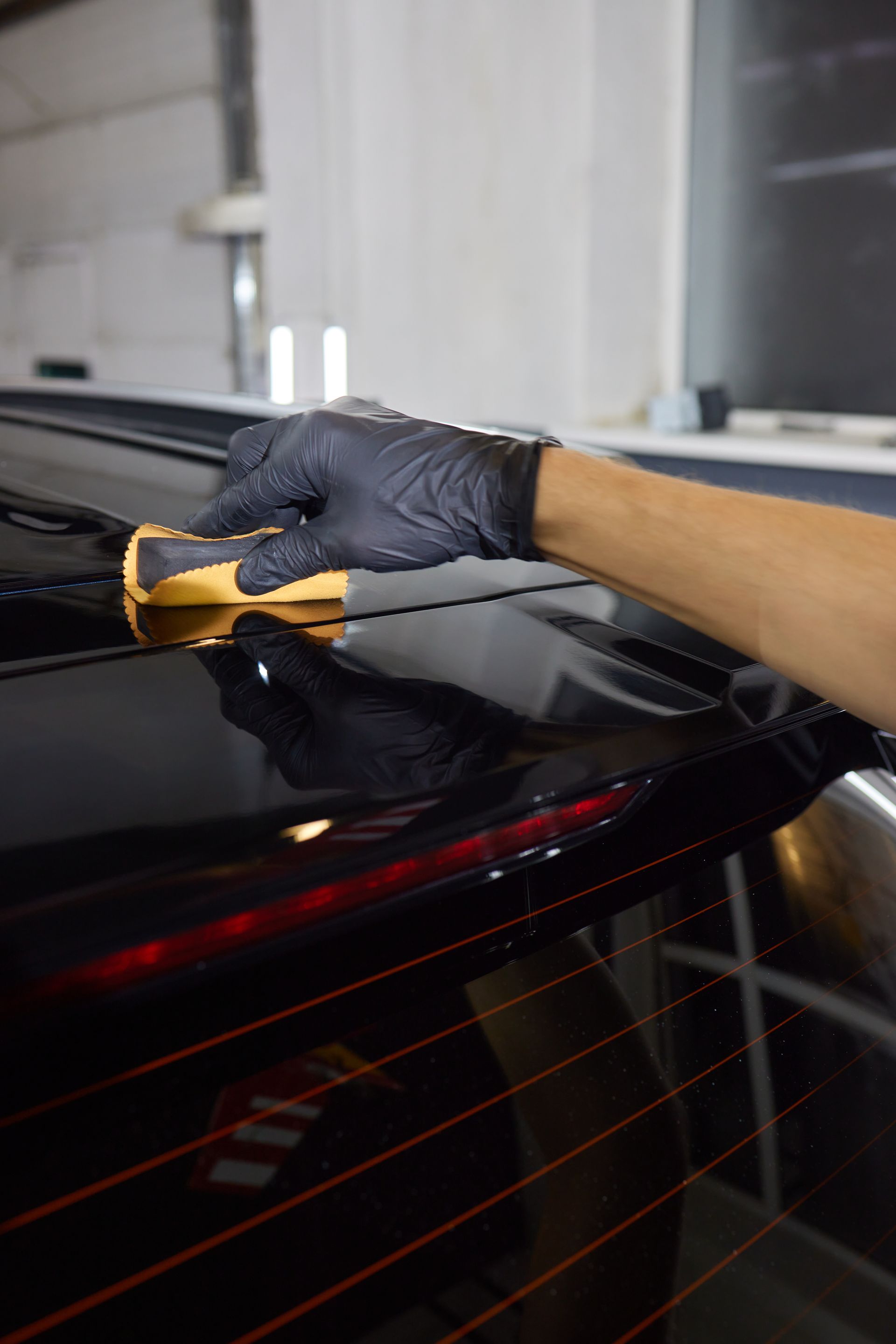 A person wearing black gloves is polishing the roof of a black car.