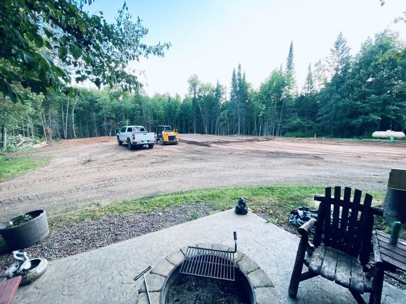 Clearing land, gravel, pickup truck, small dozer. Fire pit in foreground, trees in background.