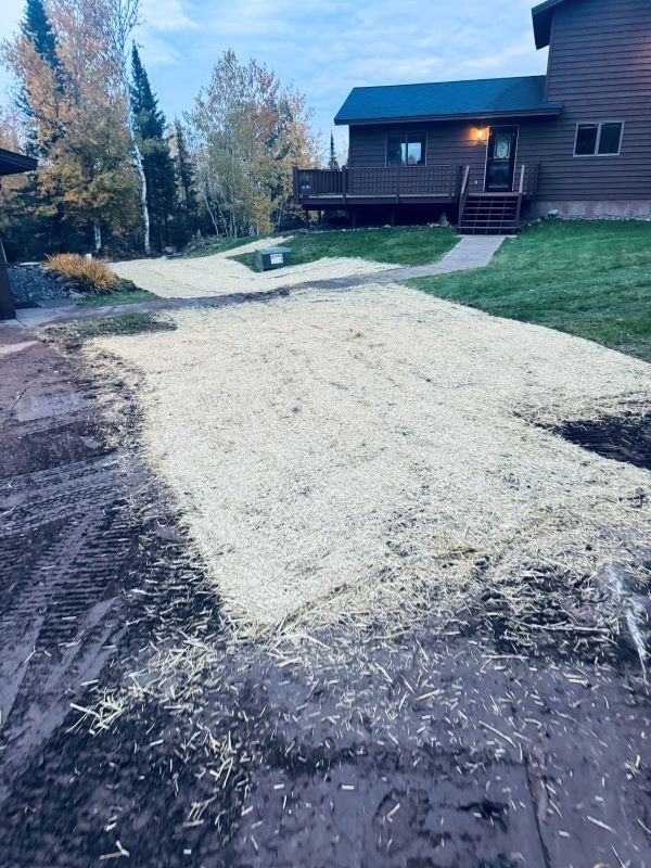 Driveway covered in straw; house in the background. Ground is dirt. Cloudy sky.