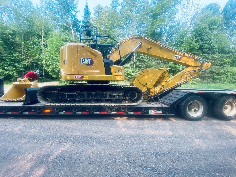Yellow Caterpillar excavator on a trailer, ready for transport. Forest background.