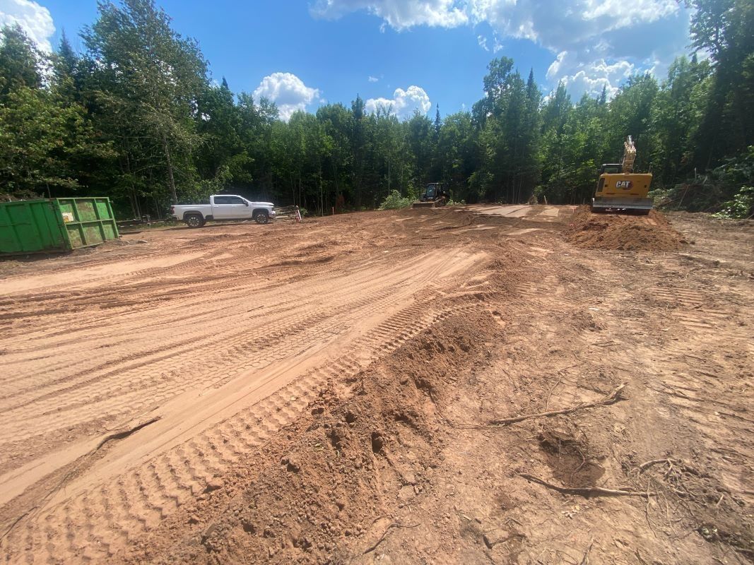 Clearing of land with a truck, excavator, and green bins under a blue sky.