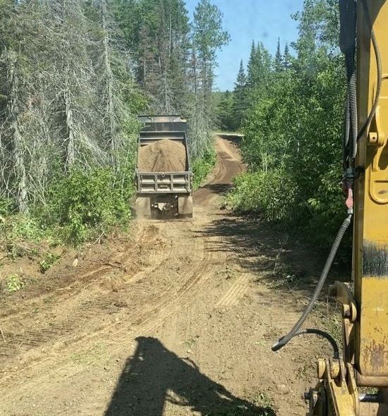 Dirt road construction: a dump truck on a muddy road in a forest, seen from heavy equipment.