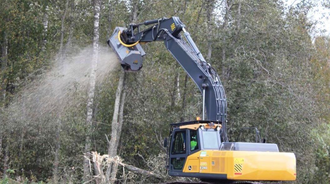 Yellow excavator mulching a tree, spraying wood chips.
