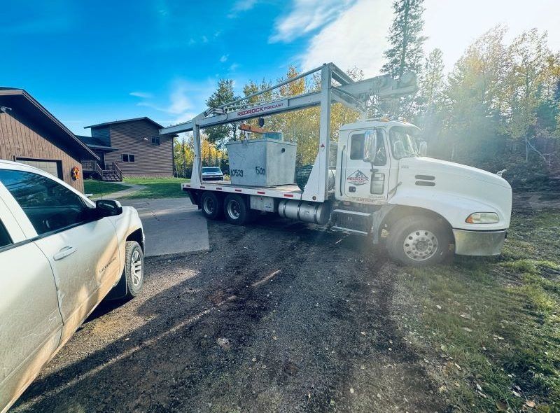 White truck with a metal frame carrying a large gray box near a house.
