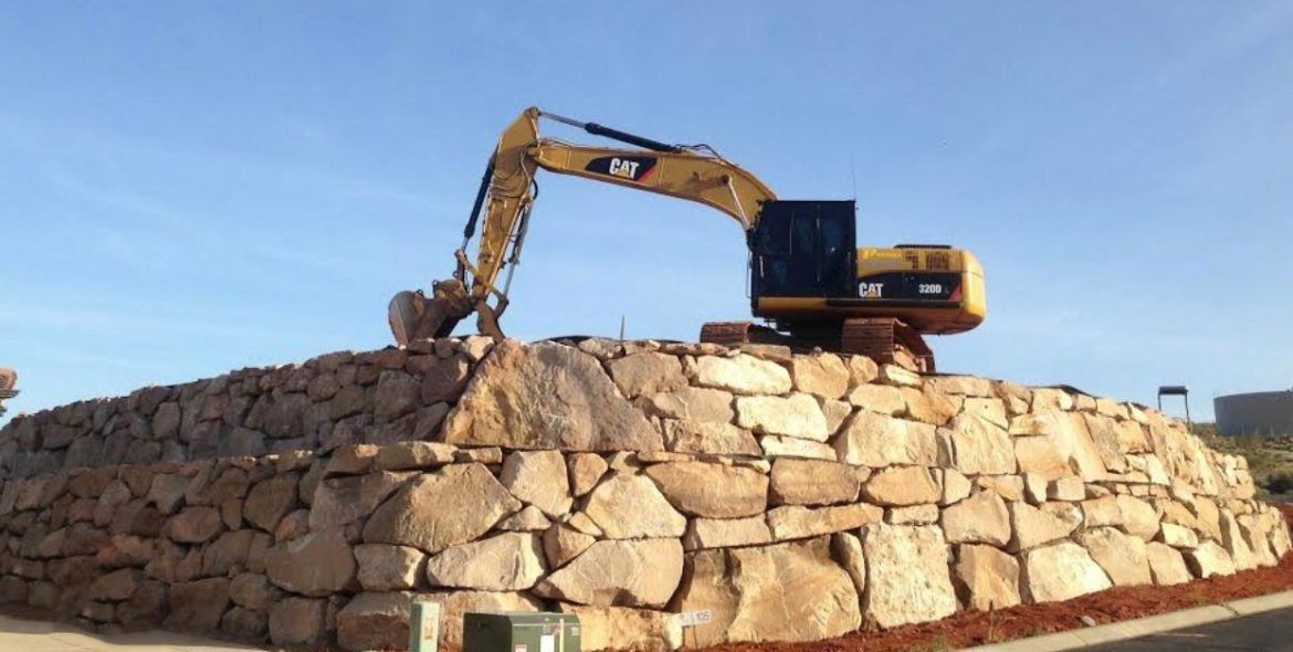 Yellow and black excavator on a large stone mound against a blue sky.