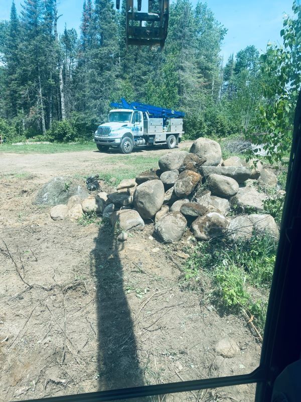 A work truck parked by a pile of rocks, likely for landscaping.  Green trees in background.