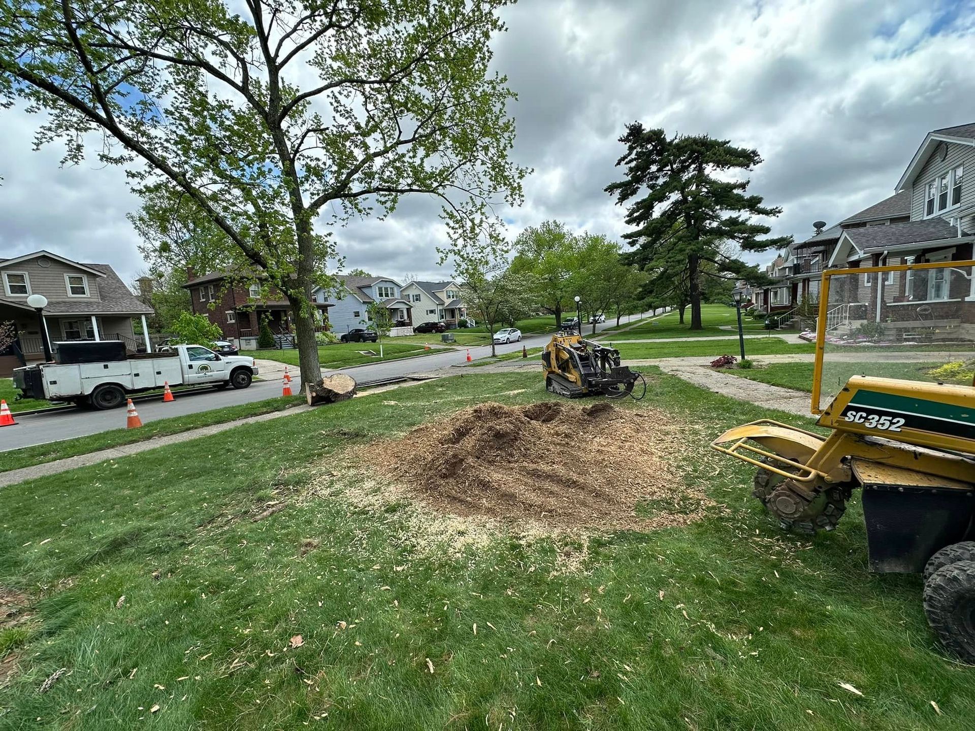 Small excavator beside a dirt mound in a grassy neighborhood park under an overcast sky
