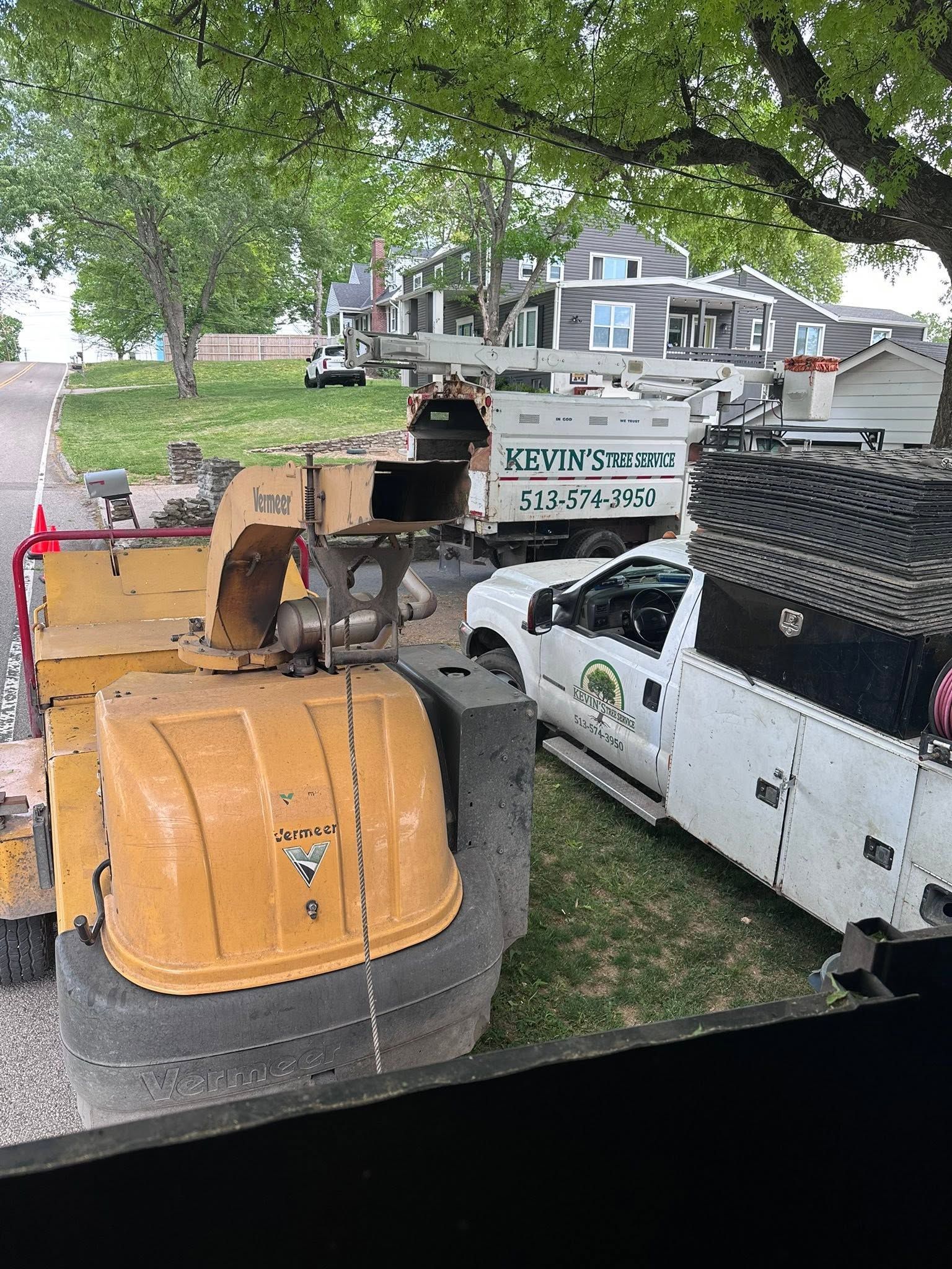 Yellow excavator beside a white work truck under trees, with a renovation sign in the background.