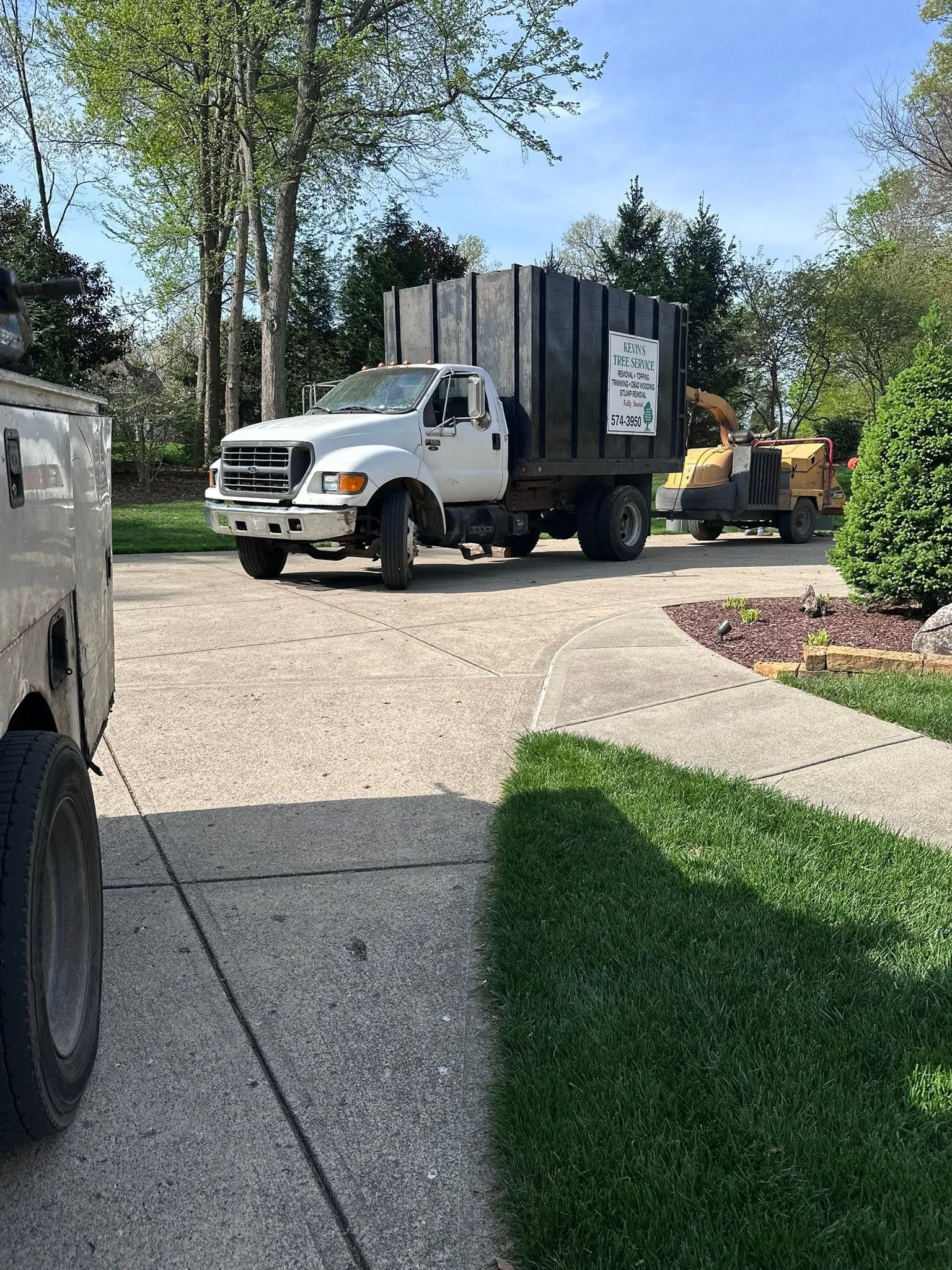 Trash truck and equipment parked on a driveway beside a lawn and trees.